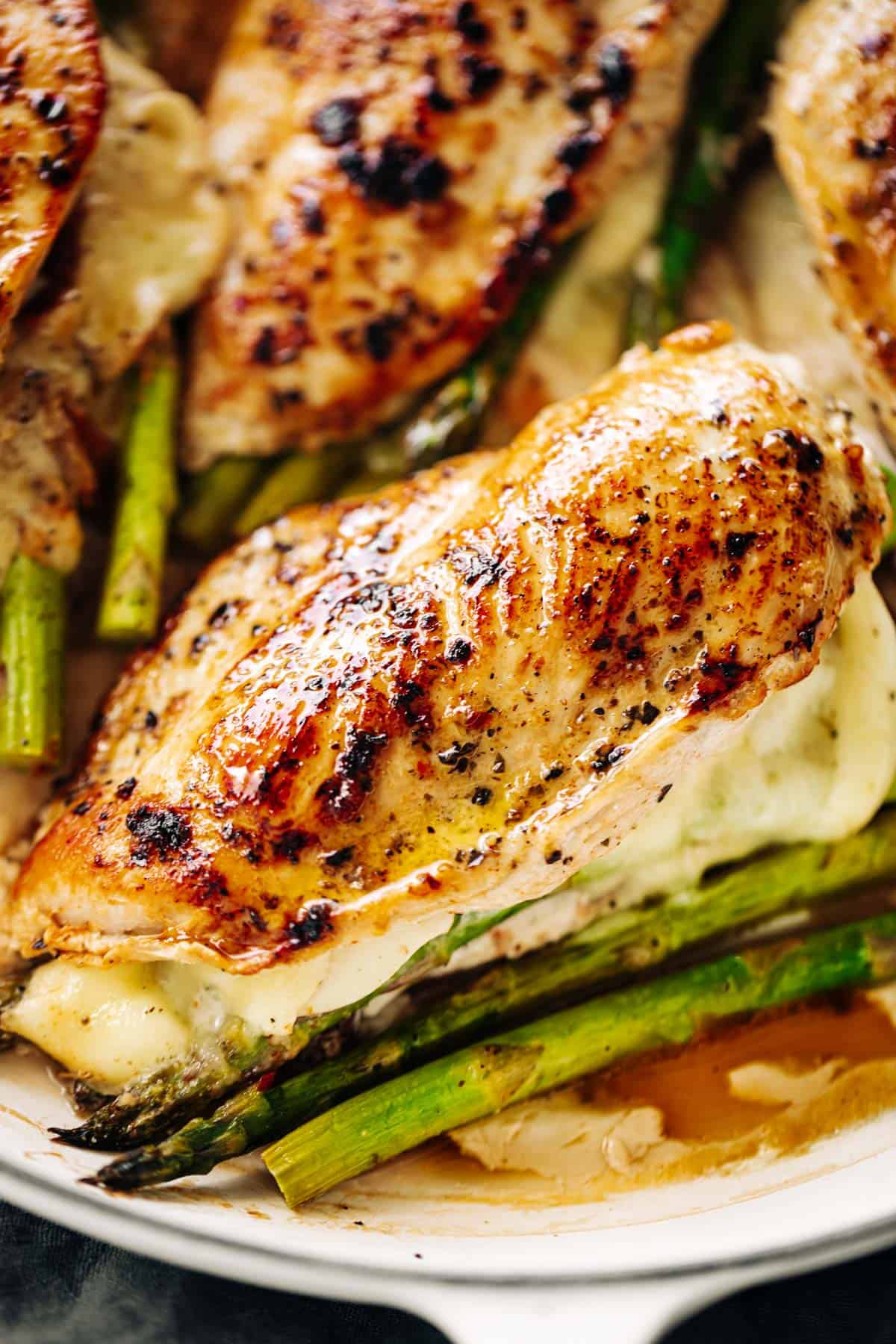 Four asparagus and mozzarella cheese stuffed chicken breasts in a white casserole dish | cafedelites.com