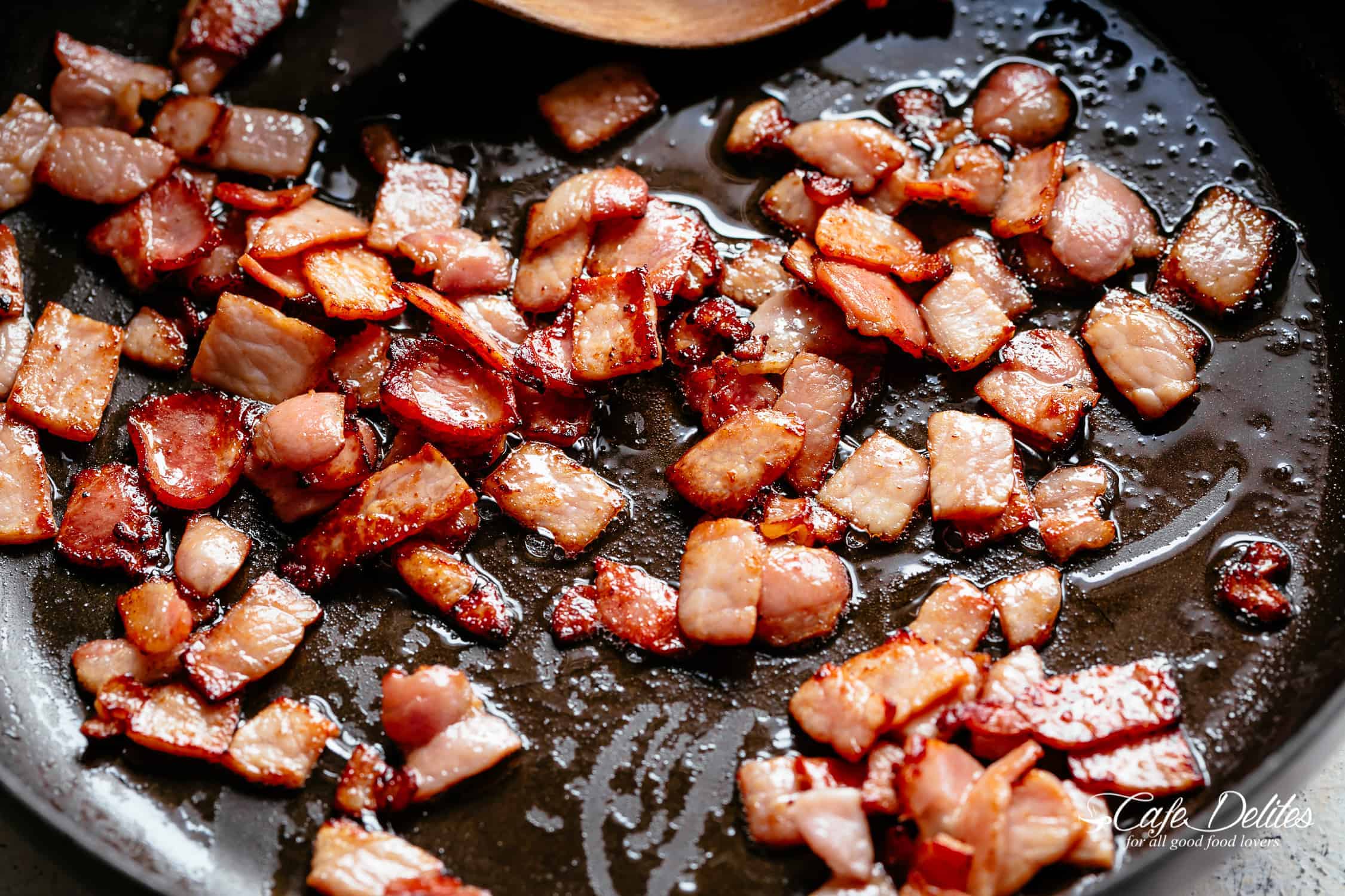 Bacon frying in a black pan with a wooden spoon | cafedelites.com