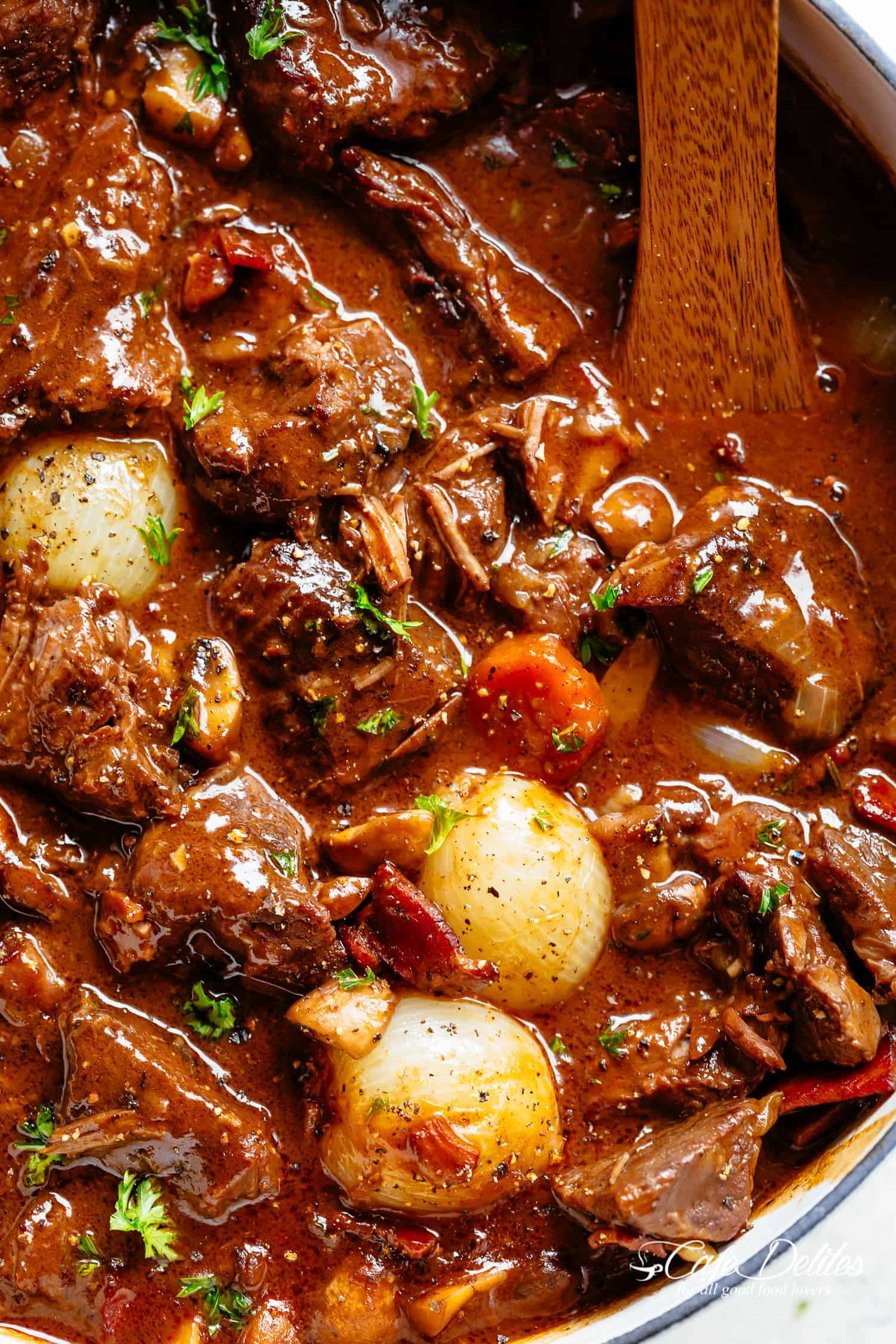 Tender beef chunks in a rich red wine gravy in a white cast iron casserole dish with a wooden spoon. | cafedelites.com