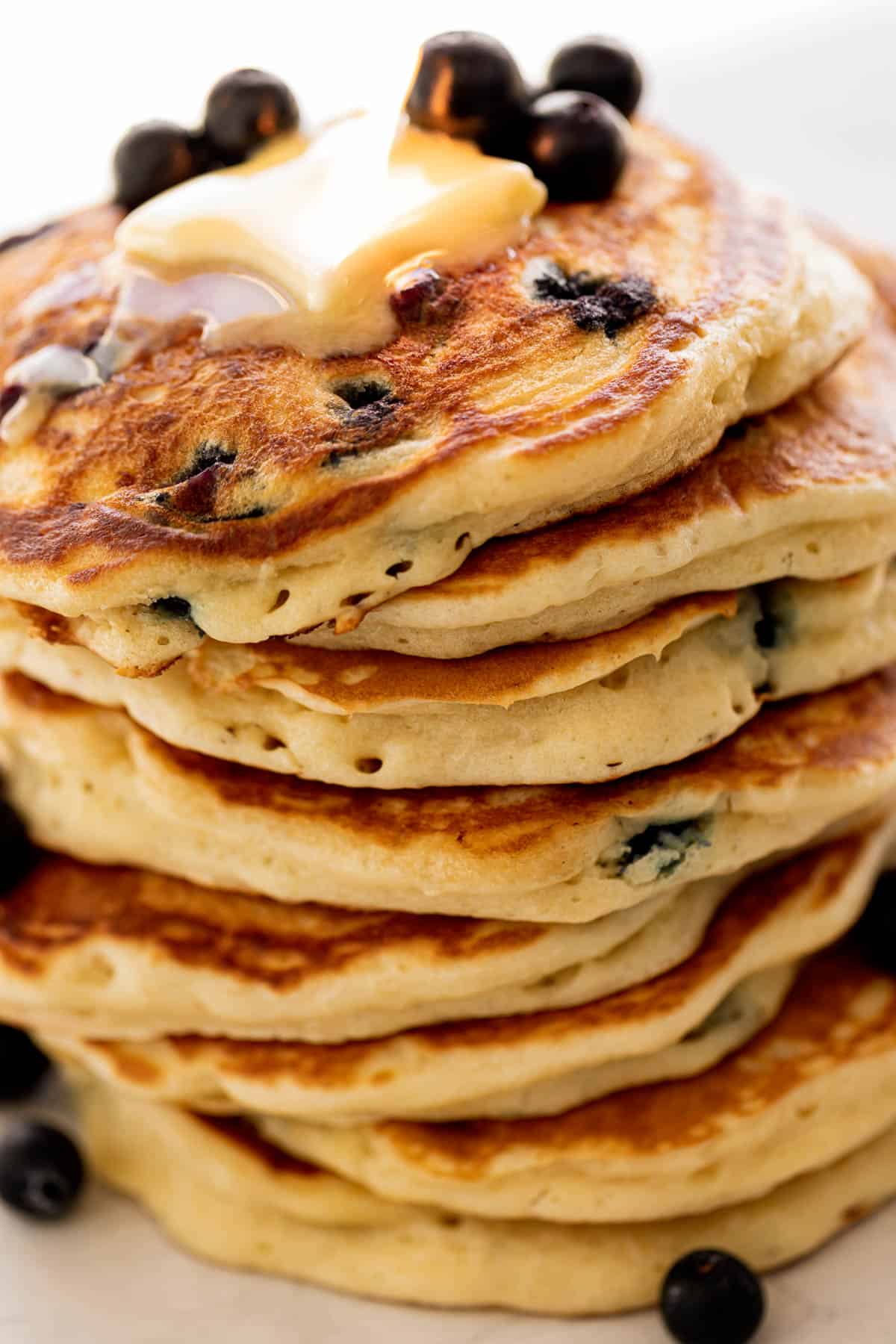 A stack of Blueberry Pancakes on a plate topped with fresh blueberries and melted butter | cafedelites.com