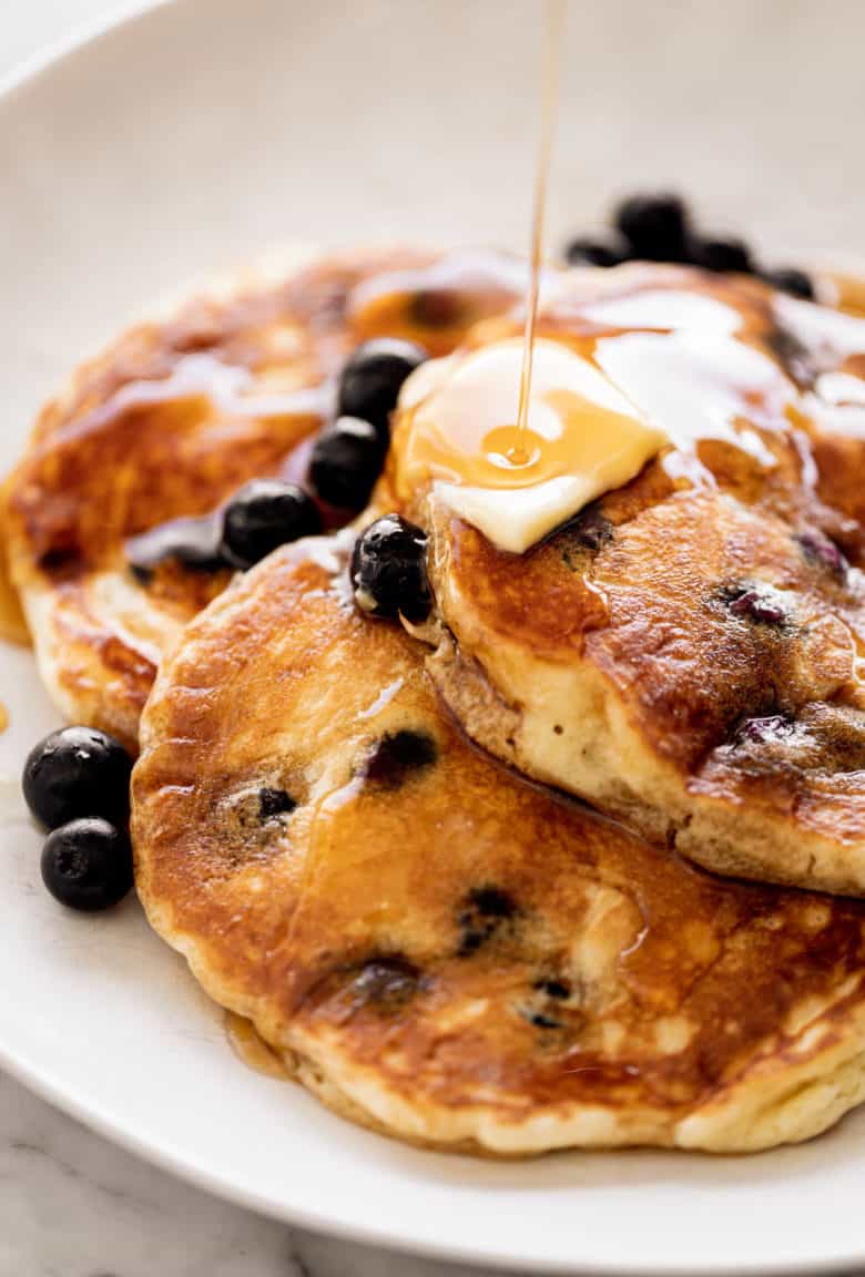 Three Blueberry Pancakes served on a plate with melted butter and maple syrup | cafedelites.com