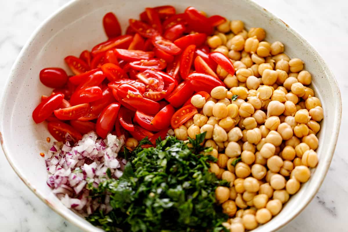 Ingredients piled in separate groups in a white bowl. From clockwise: cooked/canned chickpeas, chopped parsley, chopped red onion, quartered grape tomatoes | cafedelites
