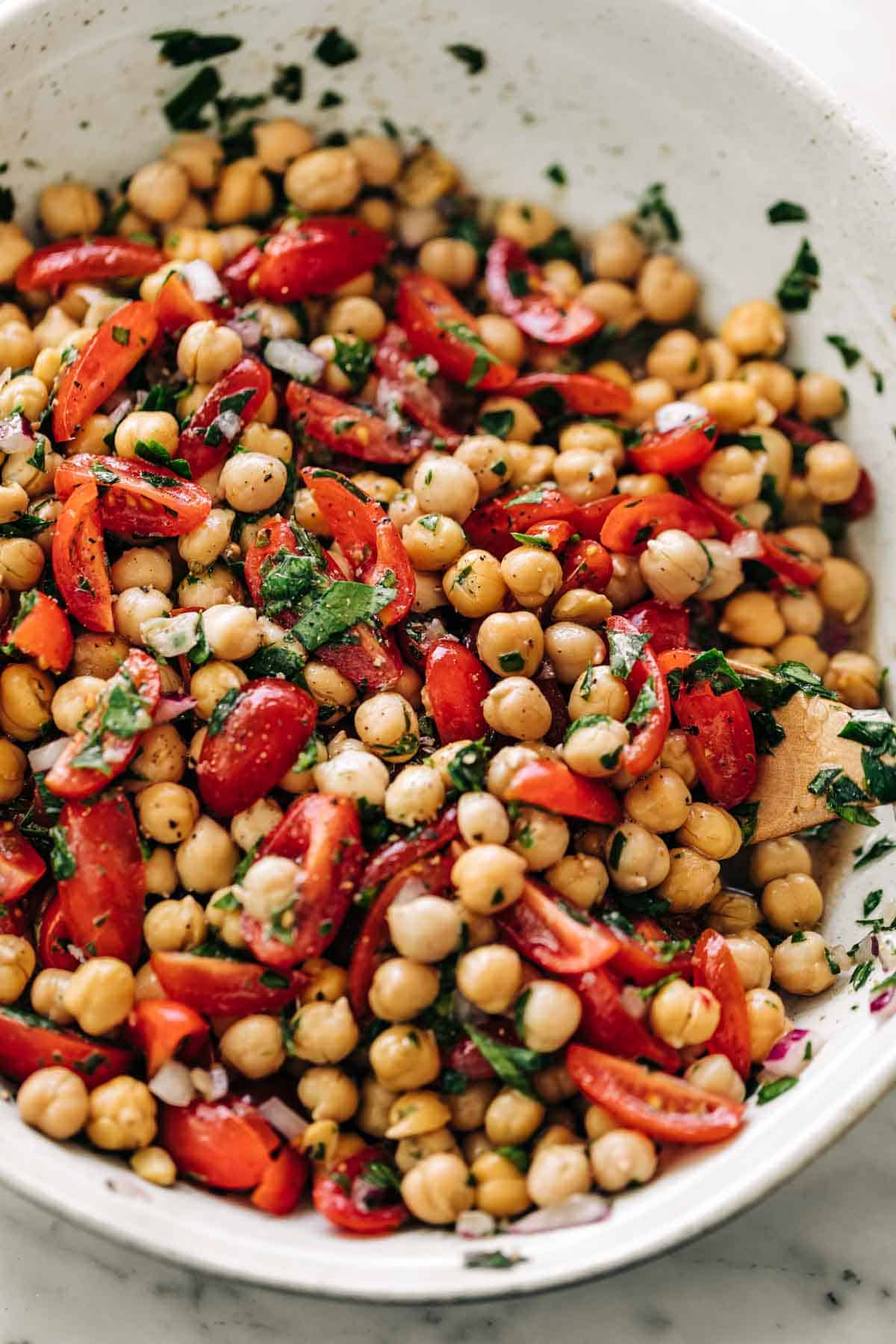 Chickpea Tomato Salad mixed with a lemon herb dressing in a white bowl on a white marble table background | cafedelites