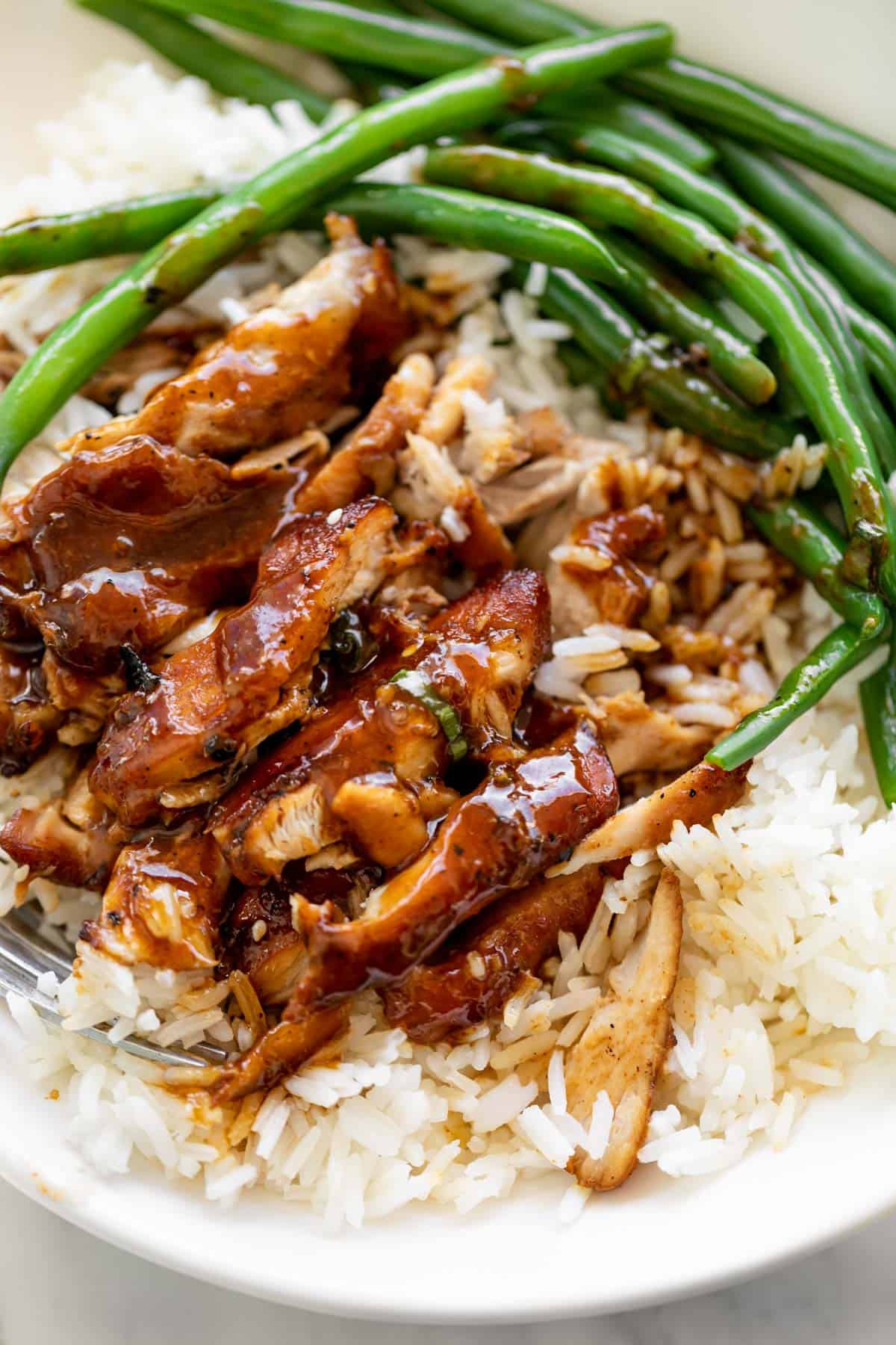 Serving suggestion: Slow cooked honey garlic chicken sits on top of plain white rice in a white bowl with sautéed green beans.