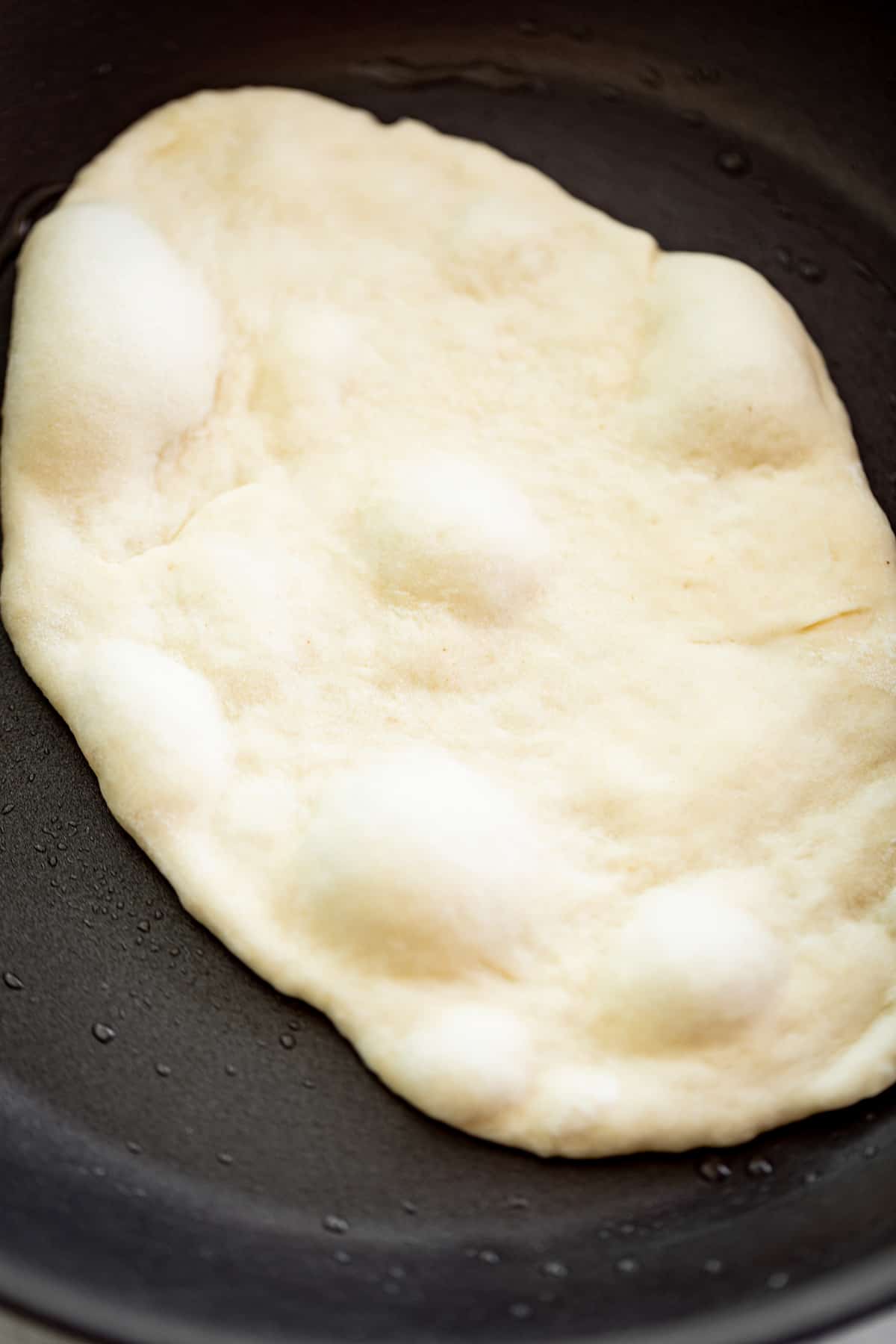 Cooking a garlic naan bread in a black skillet with a light coating of oil | cafedelites.com